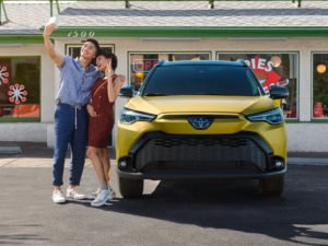 Two people taking a selfie next to a 2024 Toyota Corolla Cross parked by a storefront near Noblesville, Indiana.