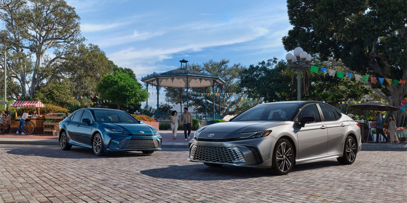 2025 Toyota Camry models parked in a scenic plaza, showcasing their sleek design, modern front grille, and stylish color options.