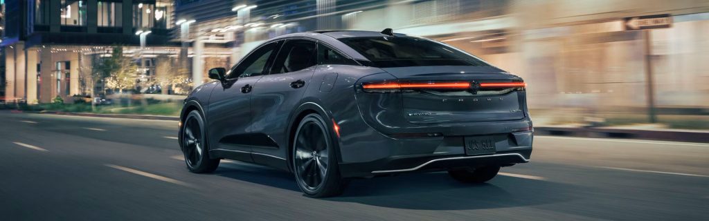 Rear view of a 2026 Toyota Crown Limited driving through a modern city street at night, showcasing sleek taillight design and aerodynamic profile