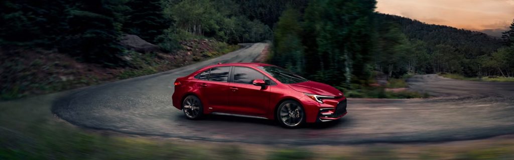 2026 Toyota Corolla in red driving on a scenic mountain road at sunset, highlighting its sleek design and smooth performance.