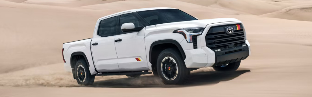 White 2026 Toyota Tundra truck driving on sandy terrain, kicking up dust.