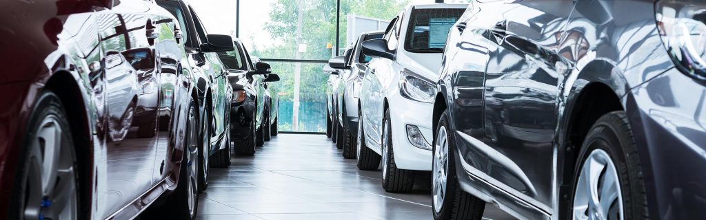 Cars lined up inside a dealership showroom with natural light coming through the windows.