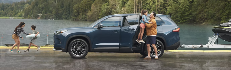 Family loading up beside a blue Toyota SUV towing a personal watercraft at a lakeside dock