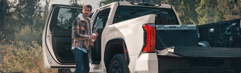 Man stepping out of a white Toyota Tundra parked on a forest trail