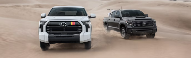 White and black Toyota Tundra pickups driving across desert sand dunes