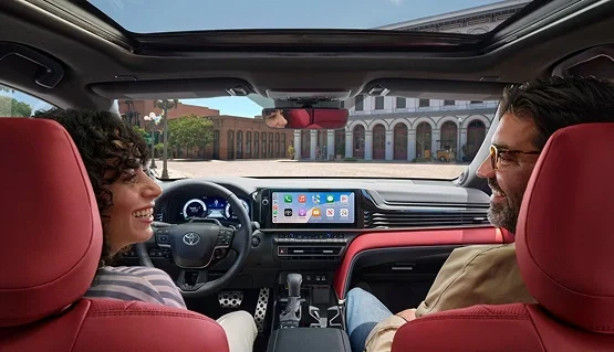 Two people smiling at each other in the front seats of a Toyota with red seats and a center touchscreen