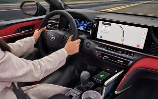 Driver's hands on the wheel of a Toyota with a red interior, beside the center touchscreen showing a map