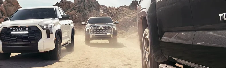 Three Toyota Tundra pickups on a dusty desert track among red rocks