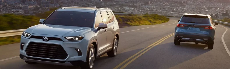 Two Toyota Grand Highlanders driving a winding hillside road above a city