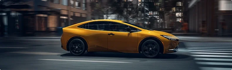 Yellow Toyota Prius driving through a city at dusk, side view