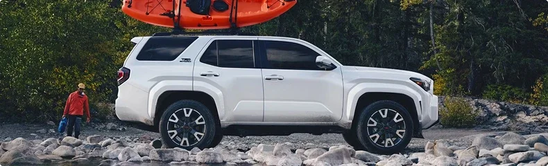 White Toyota 4Runner carrying kayaks on its roof rack, parked on a rocky riverbank