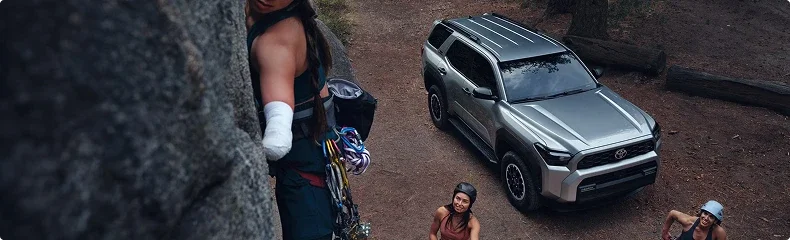Overhead view of a silver Toyota 4Runner parked at a wooded climbing spot as climbers gear up nearby