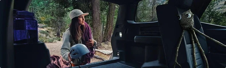 Climber loading a helmet and rope into the open cargo area of a Toyota 4Runner in a forest