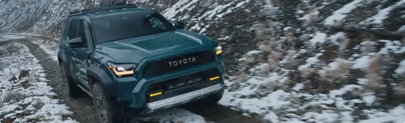 Dark green Toyota 4Runner with a roof rack working down a snow-covered mountain track