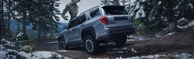 Silver Toyota 4Runner climbing a snow-dusted forest trail, seen from behind