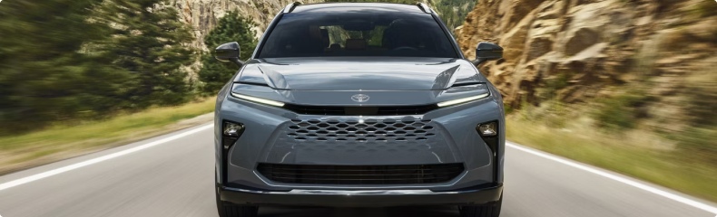 Head-on view of a gray Toyota Crown Signia driving past a rock face
