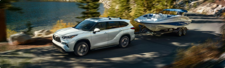 White Toyota Highlander towing a boat on a tandem trailer along a lakeside road