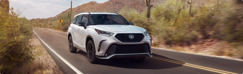 White Toyota Highlander driving a desert highway past saguaro cactus