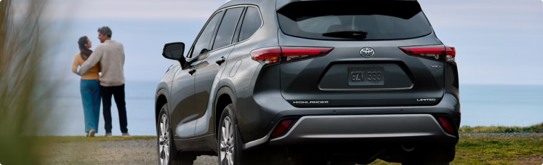 Rear view of a gray Toyota Highlander parked on a bluff as a couple look out to sea