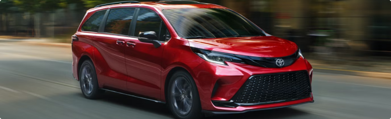 Red Toyota Sienna moving along a tree-lined city street