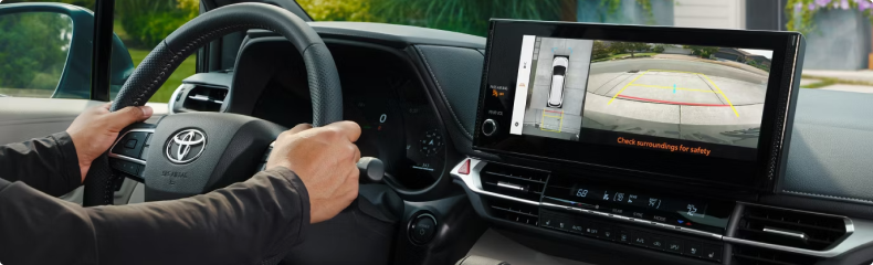 Driver at the Sienna wheel with the screen showing the overhead and reversing camera views