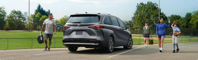 Gray Toyota Sienna parked at a ballpark as a family walks up with sports gear