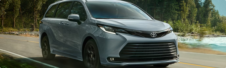 Silver Toyota Sienna on a road beside a river and evergreen forest