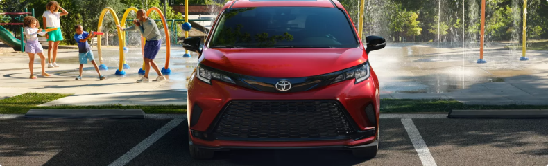 Red Toyota Sienna parked head-on beside a splash pad where children are playing