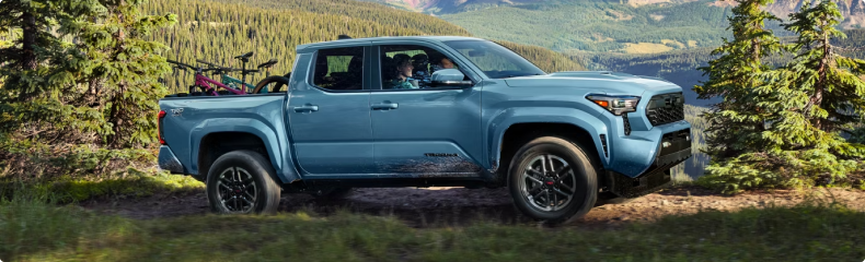 Blue Toyota Tacoma with bikes in the bed on a forest track above a valley