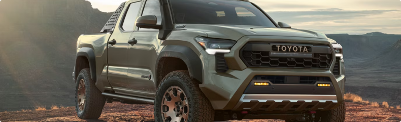 Green Toyota Tacoma Trailhunter parked on desert ground at sunrise