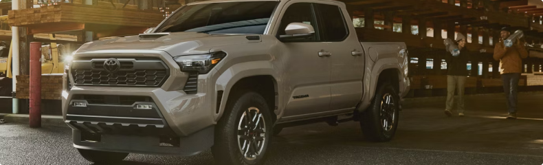 Tan Toyota Tacoma parked at a lumber yard as two workers carry timber
