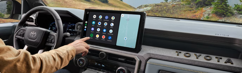Driver reaching to the Tacoma touchscreen with open country through the windshield