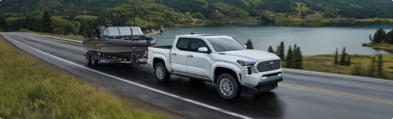 White Toyota Tacoma towing a bass boat on a tandem trailer beside a lake