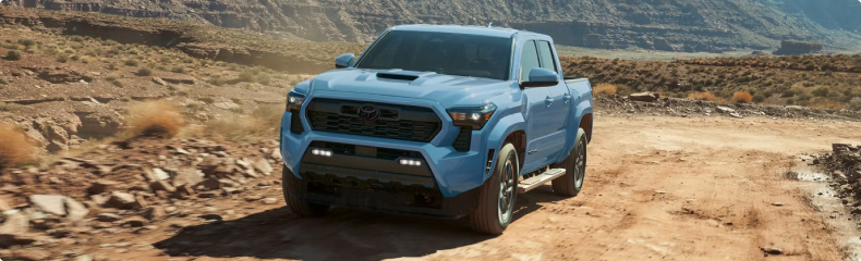 Light blue Toyota Tacoma on a desert trail with canyon walls behind it