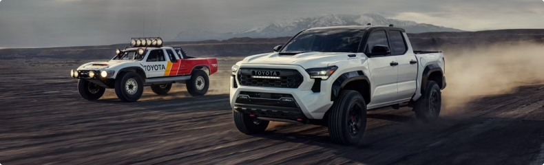 White Toyota Tacoma TRD Pro alongside a vintage Toyota race truck on open ground