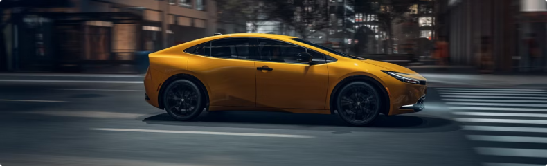 Yellow Toyota Prius in profile crossing a city intersection