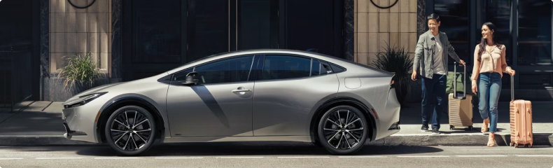 Silver Toyota Prius at a kerb as a couple approach with luggage